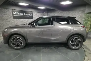 Vue de profil côté gauche du DS3 Crossback gris métallisé avec toit noir et jantes alliage 18 pouces dans un showroom.