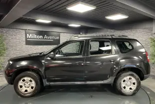 Profil côté gauche d'un Dacia Duster noir 2016 avec barres de toit et jantes acier en showroom.