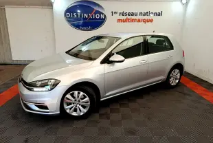 Volkswagen Golf gris clair vue 3/4 avant droit dans un showroom avec logo Distinxion en arrière-plan.