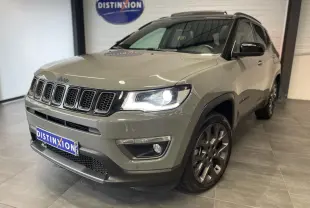 Jeep Compass gris foncé vu en 3/4 avant droit avec phares allumés et jantes alliage sombres.