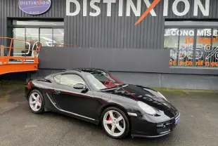 Porsche Cayman noir vue 3/4 avant droit, jantes argentées et étriers de frein rouges, stationnée devant un bâtiment.