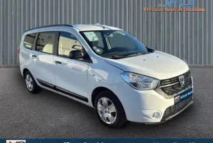 Vue 3/4 avant d'un Dacia Lodgy blanc avec barres de toit, garé devant un mur métallique.
