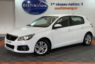 PEUGEOT 308 blanc en vue 3/4 avant droit, avec phares allumés et jantes alliage, en intérieur showroom.