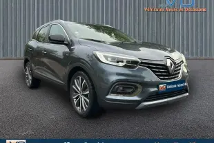 Renault Kadjar gris 3/4 avant droit avec jantes alliage 18 pouces et barres de toit visibles sur sol asphalté.