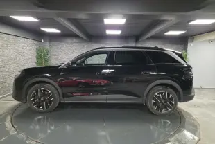 Vue de profil côté gauche d’un Peugeot 5008 noir 2025 avec jantes alliage 19 pouces et barres de toit noires.
