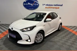 Toyota Yaris hybride blanche vue 3/4 avant droit en intérieur avec phares et antibrouillard allumés.