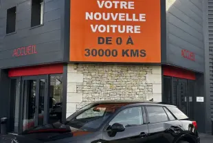 Audi Q2 noir vue 3/4 avant droit, garée devant un bâtiment avec panneau orange Distinxion.