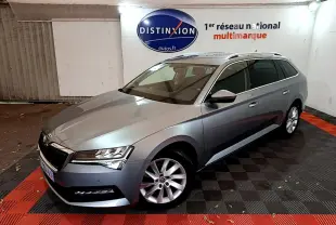 SKODA SUPERB gris clair en 3/4 avant droit, break élégant avec jantes alliage et barres de toit chromées.