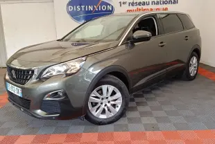 Peugeot 5008 gris foncé vue en 3/4 avant droit, avec phares allumés et jantes alliage, en intérieur showroom.