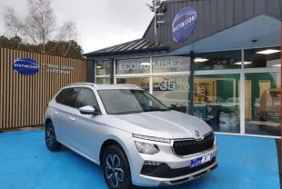 Vue 3/4 avant gauche d'un Skoda Kamiq gris diamant métallisé avec jantes alu et calandre noire devant un showroom.