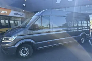 Vue de profil côté gauche d'un Volkswagen Crafter Fourgon gris foncé 2020 stationné devant un bâtiment commercial.