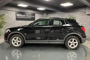 Profil côté gauche d'un Audi Q2 noir brillant 2022 avec jantes aluminium 5 branches en intérieur showroom.