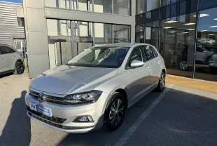 Volkswagen Polo gris métal vue 3/4 avant droit, garée devant un showroom avec jantes alliage distinctives.