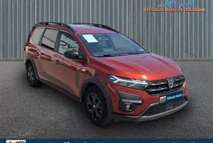 Dacia Jogger marron clair en 3/4 avant droit avec barres de toit et jantes 16 pouces noires sur parking.