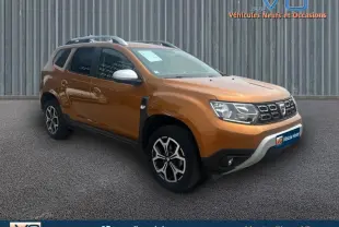 SUV Dacia Duster orange en 3/4 avant droit, avec barres de toit et jantes alliage noires et argentées.