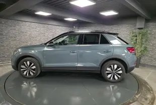 Vue de profil côté gauche d'un Volkswagen T-Roc bleu métallisé avec toit noir dans un showroom.