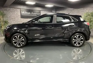 Ford Puma noir vue de profil côté gauche avec jantes alliage bicolores et toit noir brillant en intérieur showroom