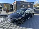 Vue 3/4 avant droite d'une Toyota Corolla Touring Sport 2.0 196 Design noire, hybride essence, sur parking extérieur.