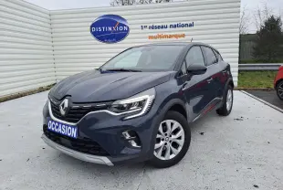 Renault Captur bleu marine en 3/4 avant droit, avec calandre distinctive et phares LED allumés, stationné devant un mur blanc.