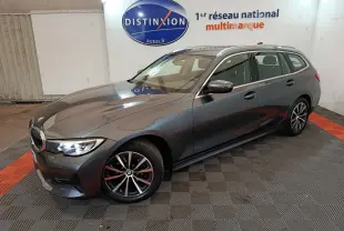 BMW Série 3 316d gris clair vue 3/4 avant droit, avec jantes alliage et phares LED allumés en intérieur showroom.