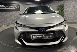 Vue frontale d'une Toyota Corolla hybride gris métallisé avec calandre noire et phares LED dans un showroom.