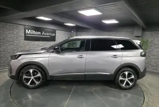 Profil côté gauche du Peugeot 5008 gris métallisé 2022 avec jantes alliage bi-ton et vitres surteintées dans un showroom.
