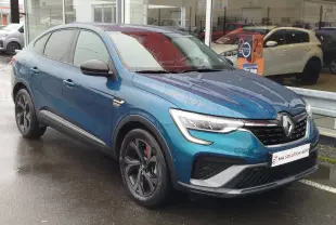 Vue 3/4 avant gauche d'un Renault Arkana 1.6 E-Tech bleu Zanzibar, avec jantes noires et détails rouges sous la pluie.