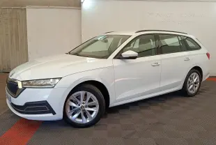 Skoda Octavia break blanc vue de profil droit en intérieur, avec jantes alliage et barres de toit noires.