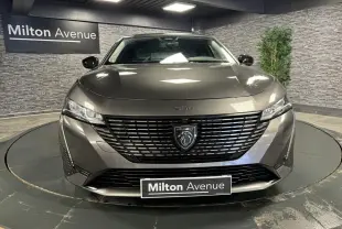 Vue frontale d'une Peugeot 308 SW gris métallisé avec calandre noire et logo lion central lumineux.