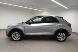 Profil côté gauche du Volkswagen T-Roc 2023 gris pyrite avec toit noir et vitres arrière surteintées en intérieur neutre.