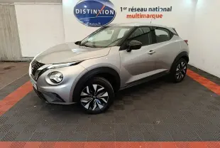 Nissan Juke gris clair en 3/4 avant droit, avec jantes noires et grises, dans un showroom intérieur.