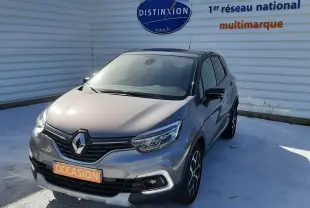 Renault Captur gris cassiope avec toit noir, vue 3/4 avant droit, sur parking devant un mur blanc marqué Distinxion.