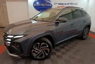 Vue 3/4 avant droit du Hyundai Tucson 1.6 Hybrid gris foncé avec jantes au design géométrique et feux LED allumés.